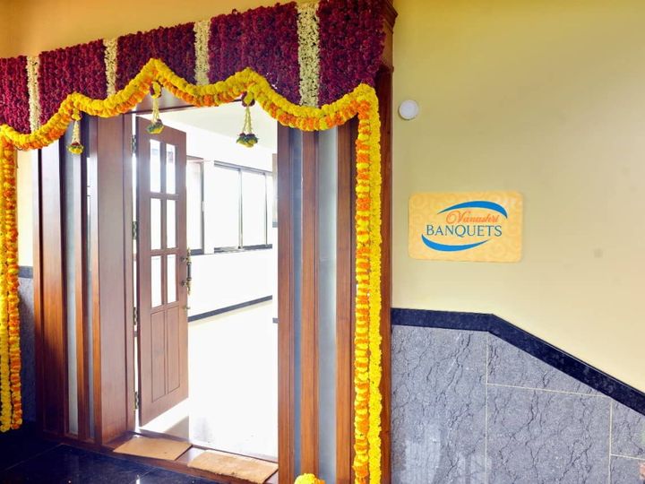 Doorway to the hall framed with marigold garlands, with a Vanashri Banquets sign on the wall