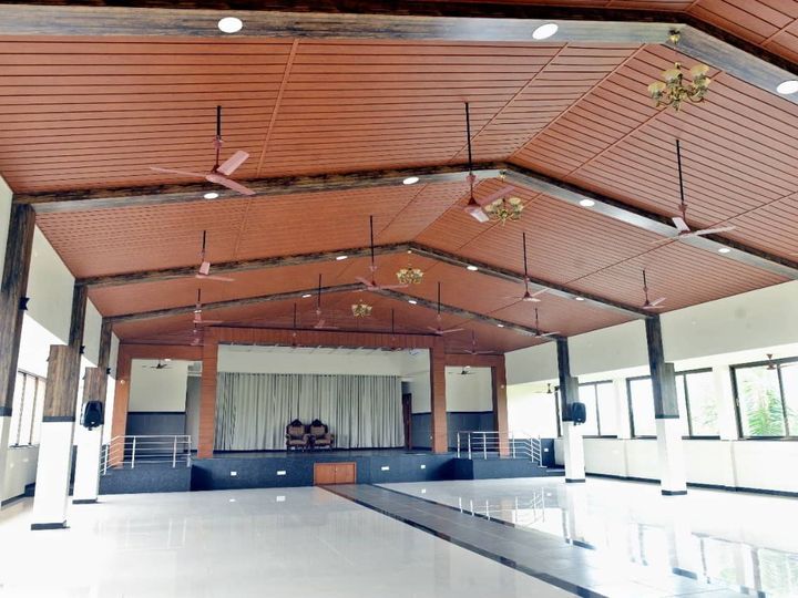 Large banquet hall with a sloping wooden ceiling, ceiling fans and the stage at the far end