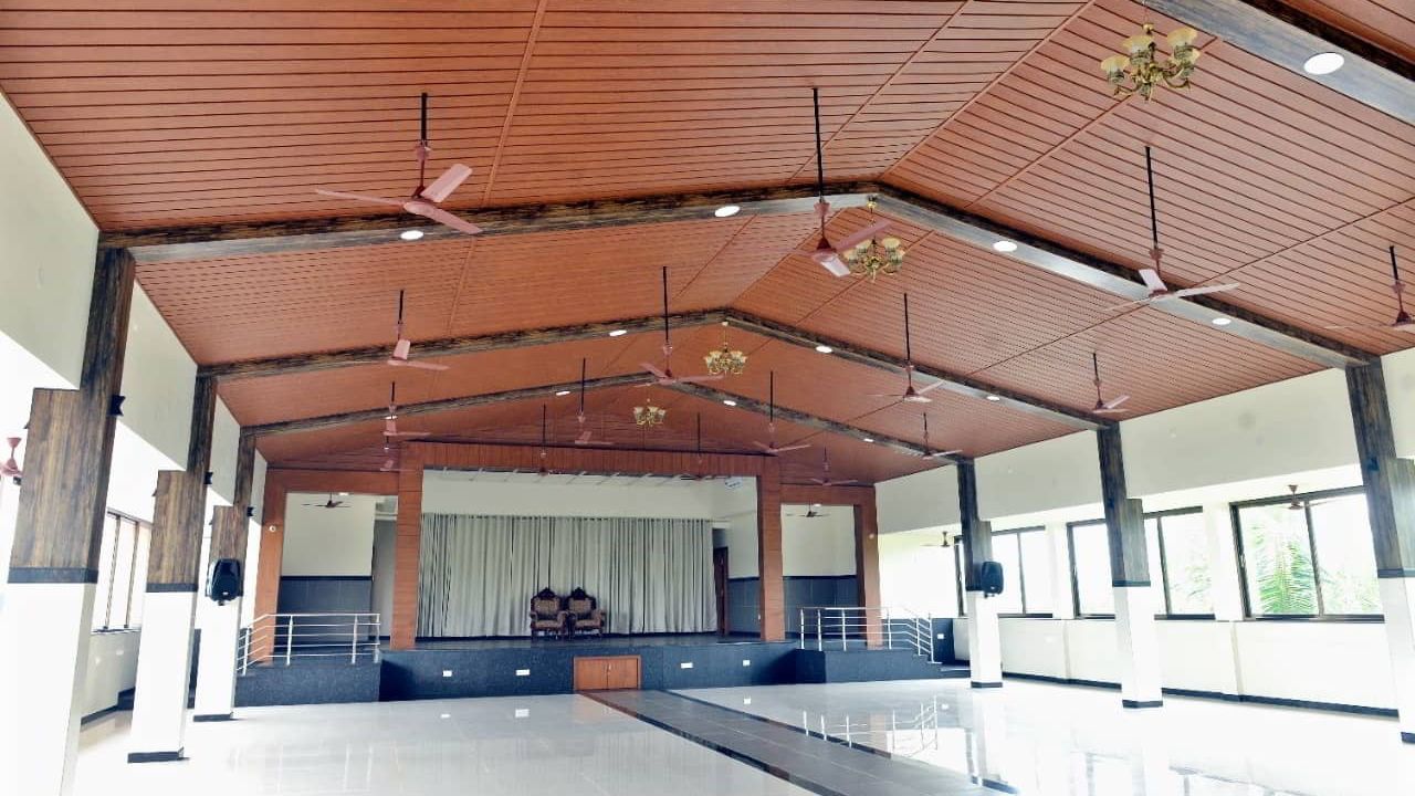 Large banquet hall with a sloping wooden ceiling, ceiling fans and the stage at the far end