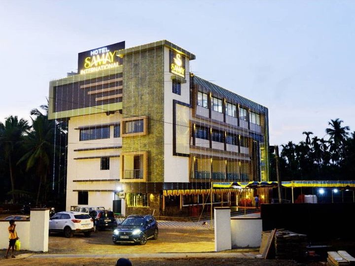 The hotel at dusk with the lit Samay International sign on top and two cars parked in front