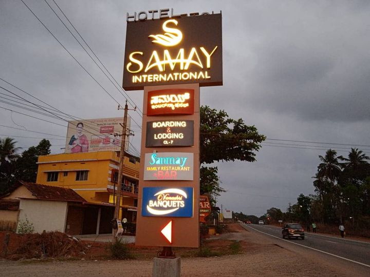 Tall roadside sign for Hotel Samay International listing boarding and lodging, the family restaurant and bar, and Vanashri Banquets