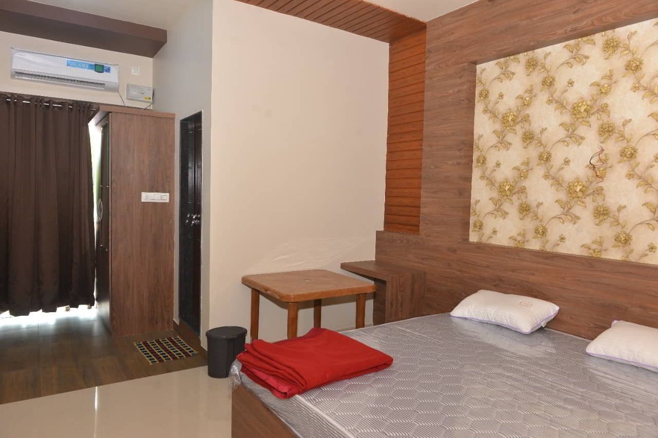 Double bed with a folded red blanket, a split air conditioner above the curtain, a side table and a patterned feature wall