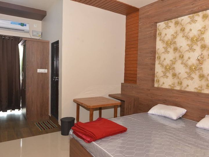 Double bed with a folded red blanket, a split air conditioner above the curtain, a side table and a patterned feature wall