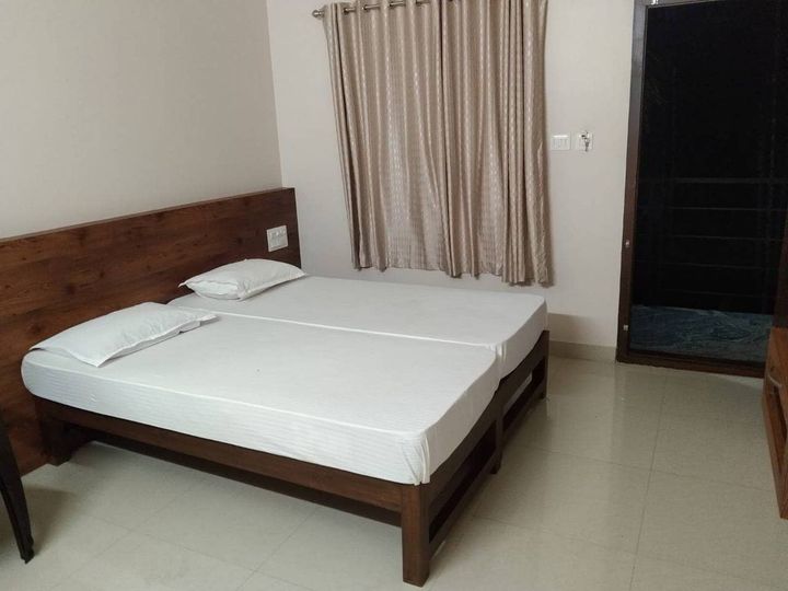 Two single beds side by side with a wooden headboard, curtains and a window